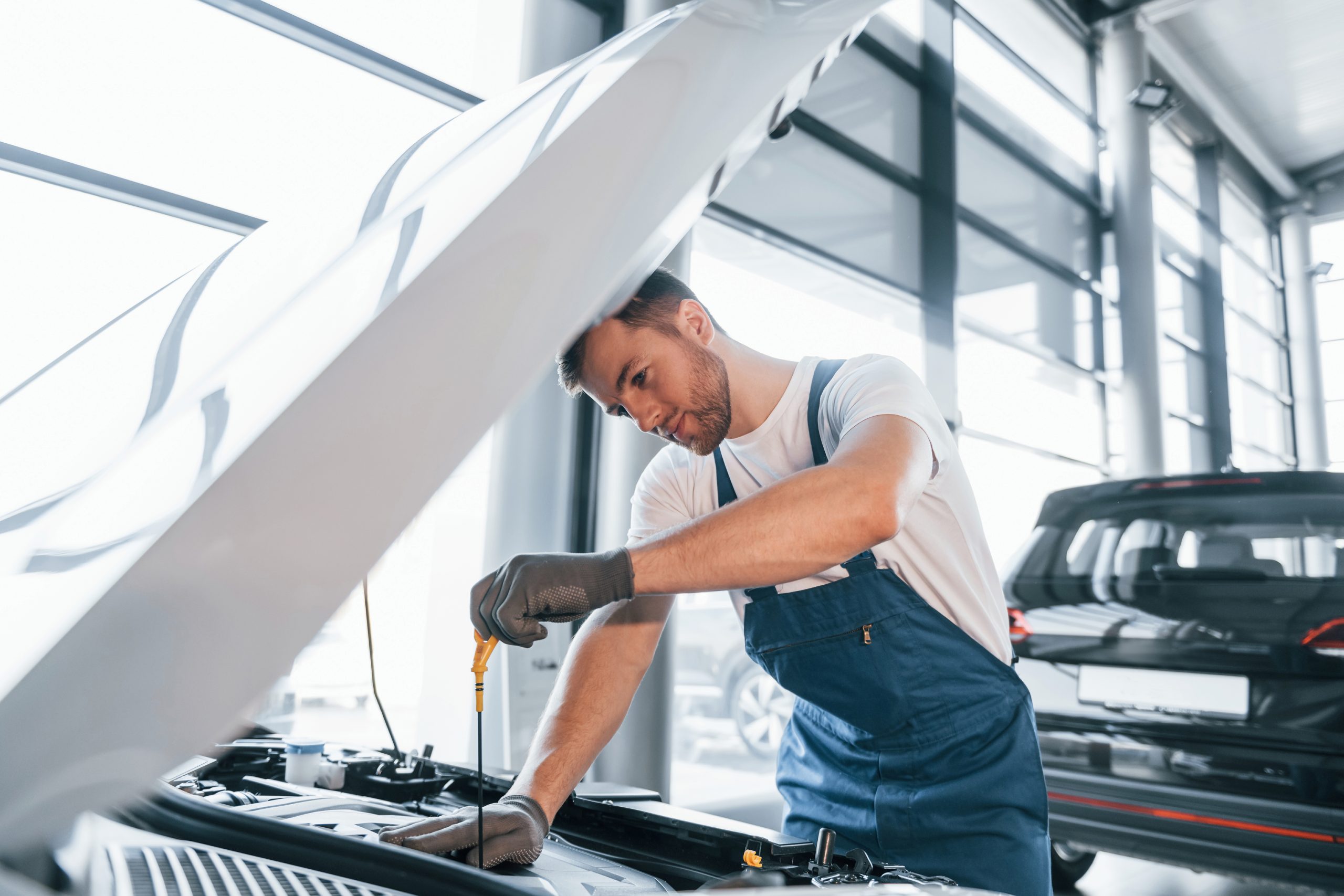 Quality service. Young man in white shirt and blue uniform repairs automobile